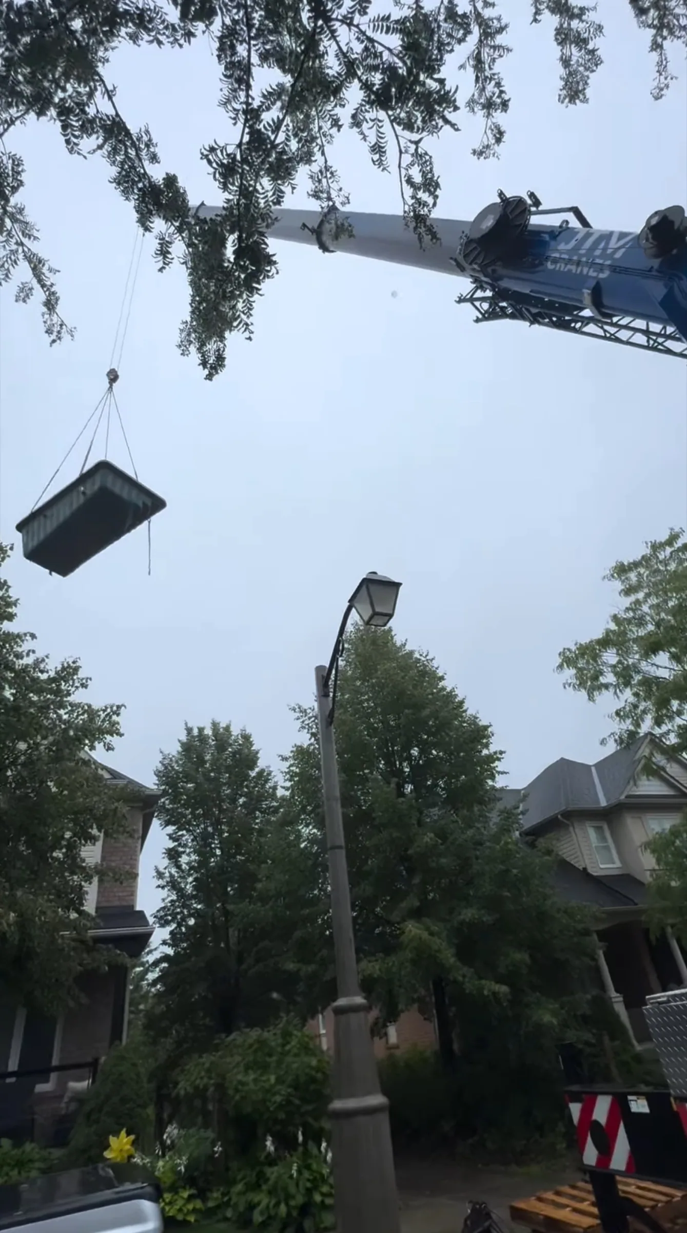 Load flying on a crane line over trees into a residential backyard