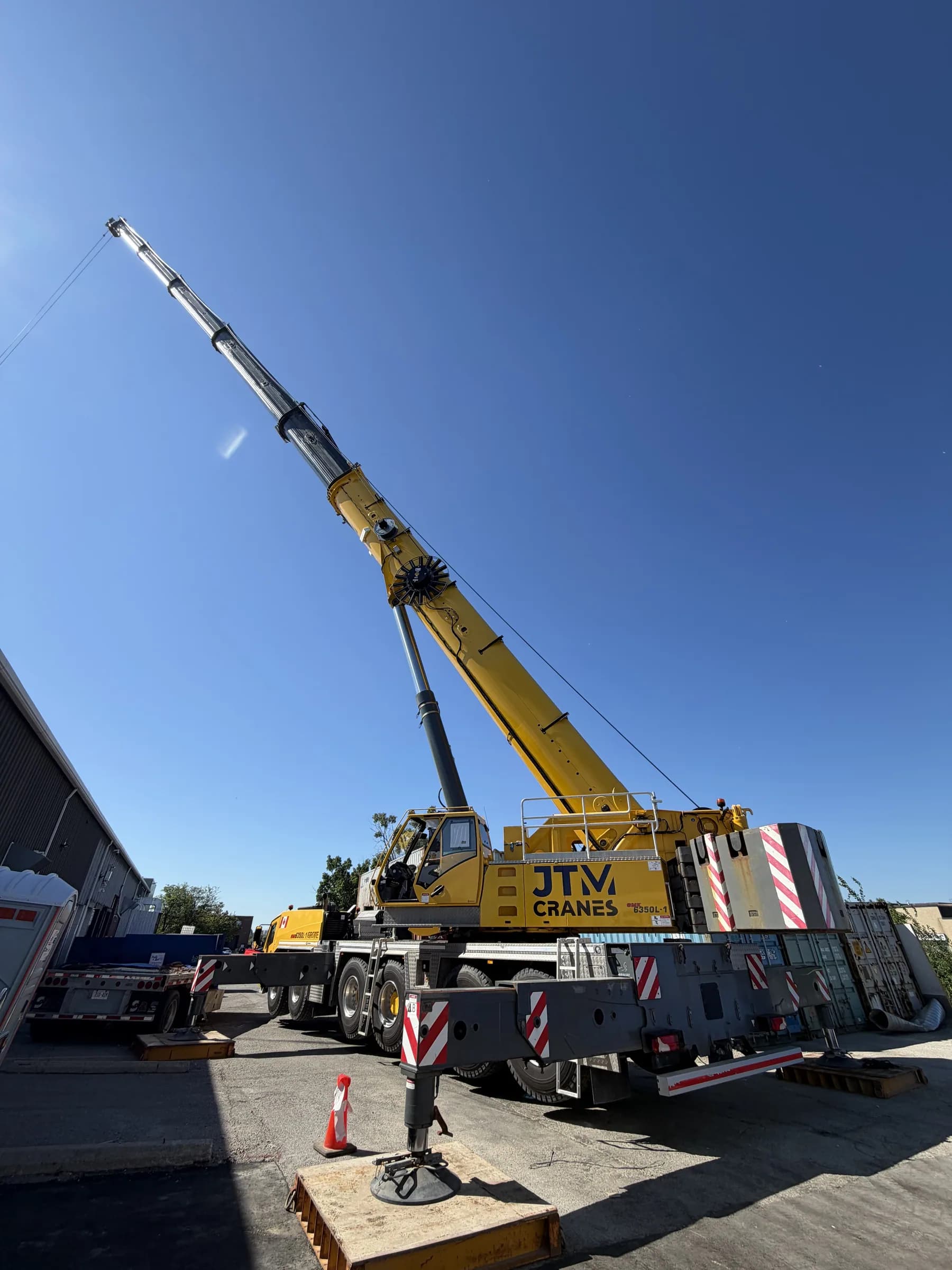 JTM Cranes yellow Grove all terrain crane set up on outriggers with the boom raised