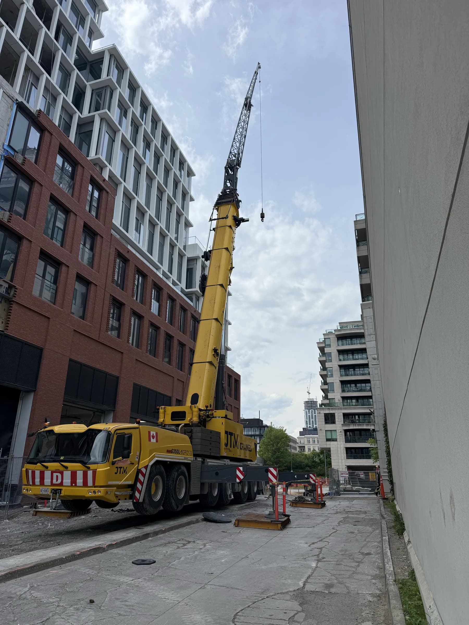 Crane set up in a tight space between two buildings, boom raised over the site
