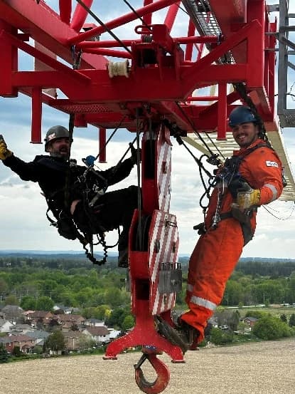Two riggers in high-visibility gear working on a tower crane at height